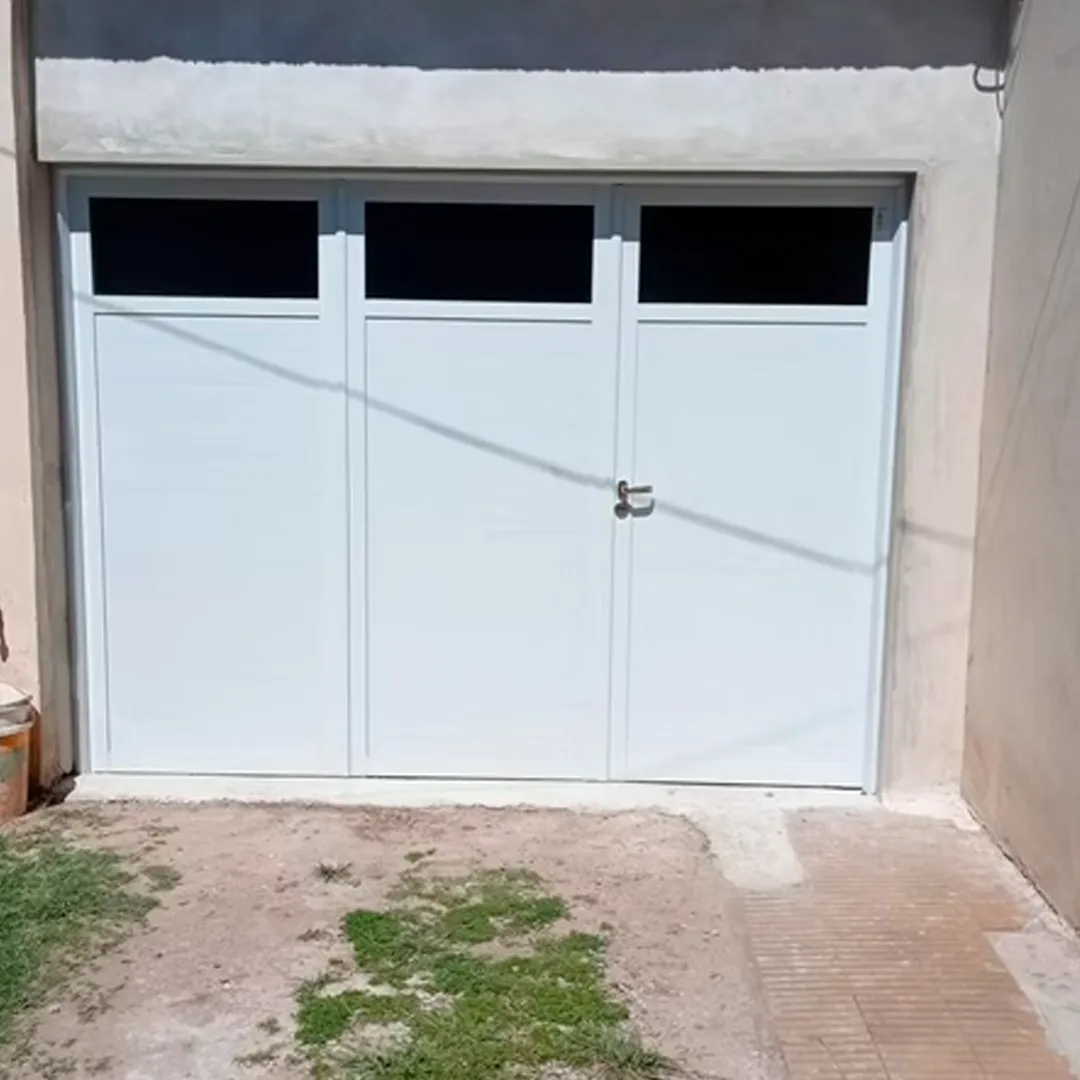 Portón de tres hojas en aluminio blanco con diseño de paños ciegos y vidriados superiores